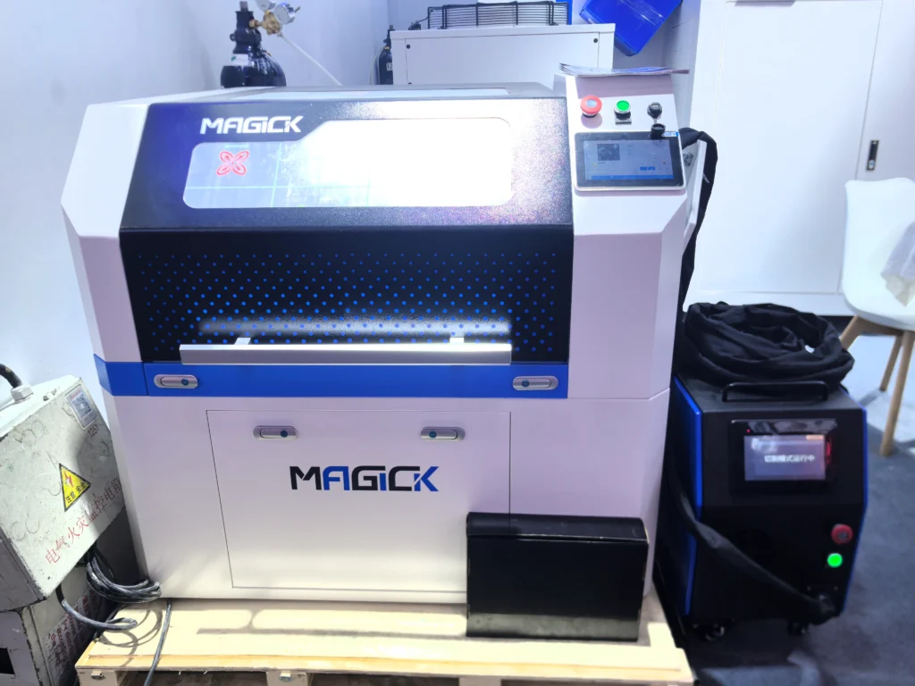 Front view of the Magick MK-B4 4-in-1 CNC Fiber Laser System on display, featuring the main enclosed CNC workstation, the external laser source unit, and the electrical control box.